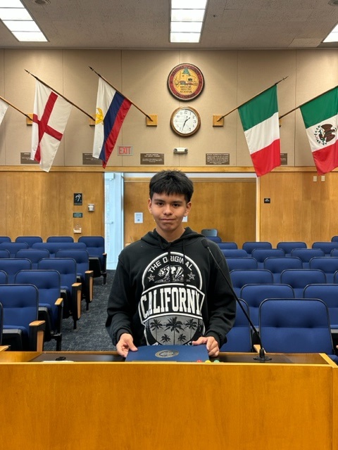 Esteban standing at a podium at the chambers with flags displayed in the background