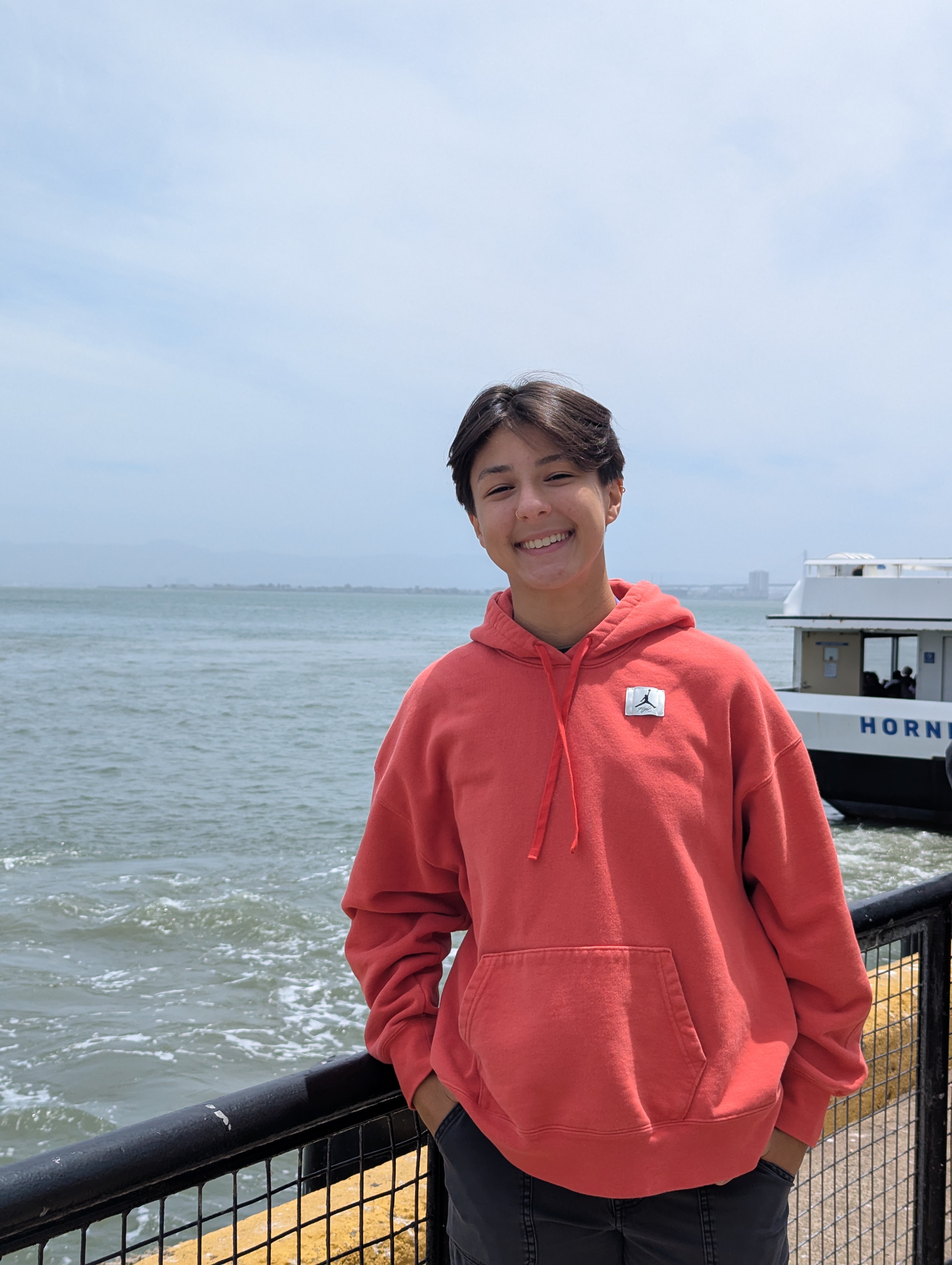Maya standing at the pier with ocean and a boat in the background
