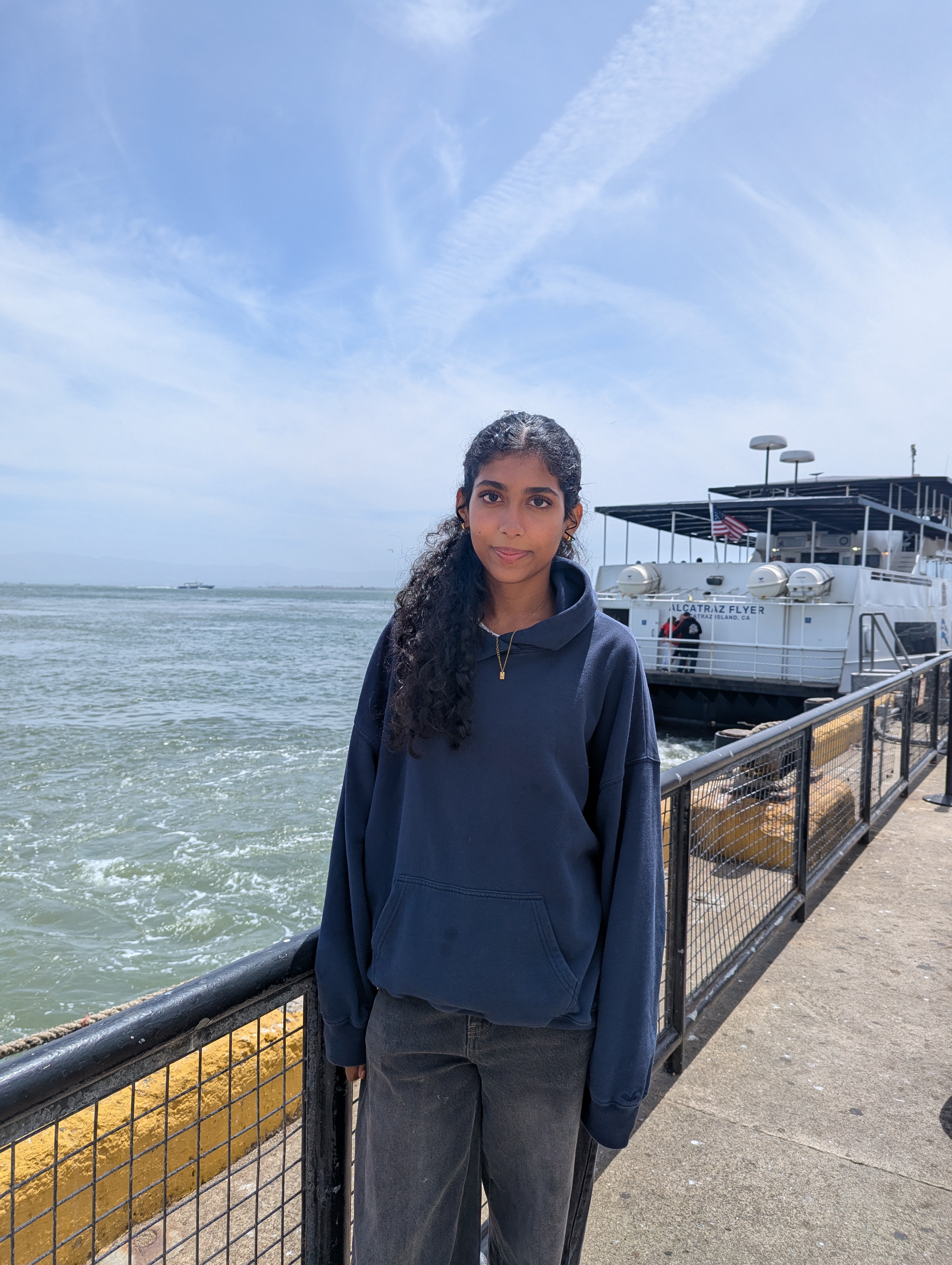 Varnika at the pier with the ocean and a boat in the background