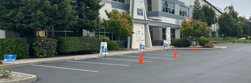 A picture of a row of parking spaces that are blocked off by orange cones for curbside voting.
