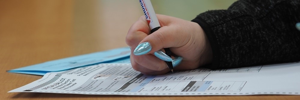 Picture of a hand voting a ballot on a desk