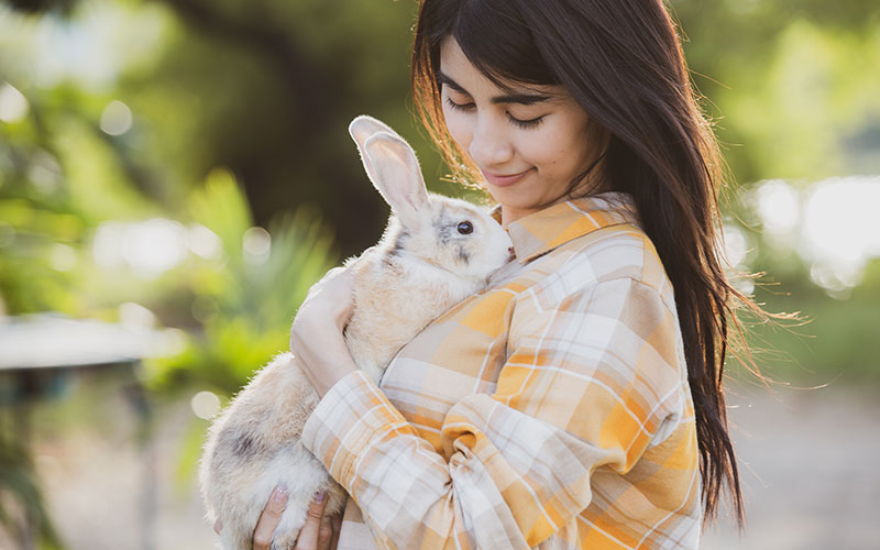 Young woman holding a white bunny with gray and tan areas outside