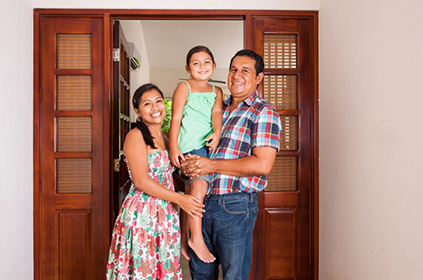 Young latino family standing at the front door of a house